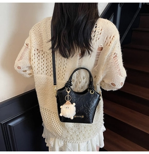 Detail of black pleated glossy bucket bag with cute plush sheep charm and metallic logo