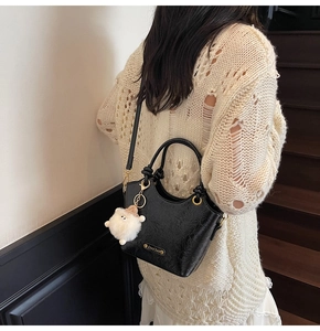 Macro detail of black glossy textured handbag with white plush charm on a wooden staircase