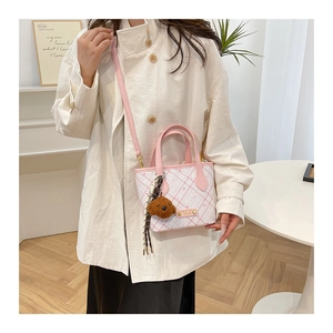 Detail of a white and pink plaid bucket bag with a plush dog charm and gold metal logo