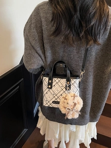 Contrast color checkered bucket bag with plush rabbit charm worn by a model in interior setting
