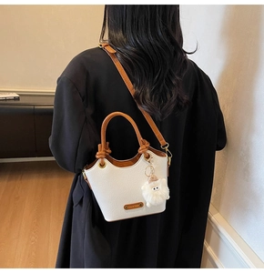 White textured bucket bag featuring brown leather straps and a plush cat charm detail