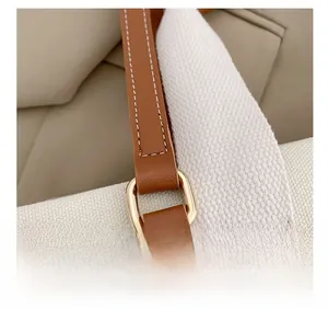 Détail de la boucle dorée avec bandoulière en cuir marron sur un sac en toile blanc
