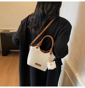 Detail of cream bucket bag with litchi grain texture and plush doll charm on a model