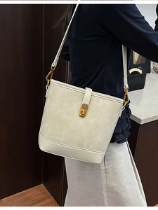 Elegant off-white bucket bag with gold lock shown in a lifestyle indoor setting