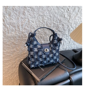 Detail of blue denim checkered bucket bag with frayed edges and silver twist lock