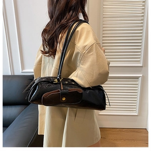 Model showing side view of black patent leather baguette shoulder bag with gold hardware