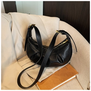 Détail du sac demi-lune en cuir grainé noir avec fermeture éclair dorée sur canapé