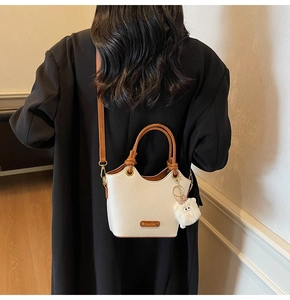 Close-up of white leather bucket bag with brown straps and plush monster charm decoration