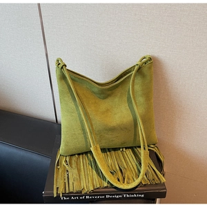 Dettaglio borsa a tracolla in pelle scamosciata verde con lunghe frange bohémien su libro