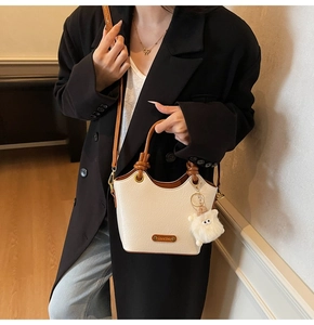 Detail of white textured leather bucket bag with brown strap and plush doll pendant