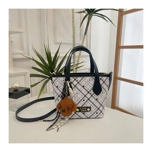 Close-up of black and white checkered bucket bag with leather trim and teddy bear charm