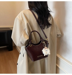 Detail view of coffee leather bucket bag with cute sheep charm on a beige trench coat