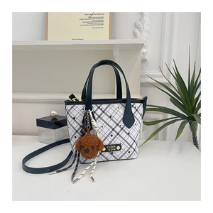 Detail showing checkered tote bag with brown teddy bear charm and sleek black handles