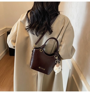 Detail of dark brown glossy bucket bag with retro pleated texture and plush charm