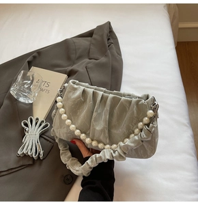 Détail du sac nuage plissé gris avec chaîne en perles et bandoulière sur lit blanc