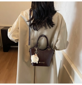 Detail of dark brown glossy leather bucket bag with a plush lamb charm and logo