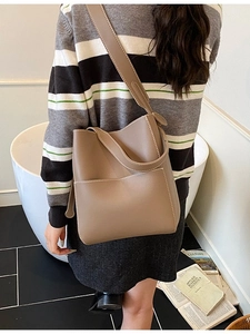 Minimalist leather bucket bag with white contrast stitching and wide shoulder strap
