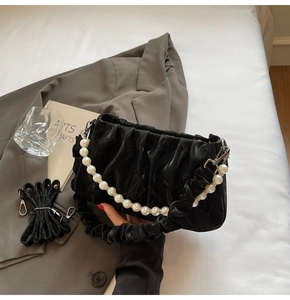 Détail d'un sac nuage plissé noir avec chaîne en perles et bandoulière sur fond blanc
