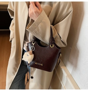 Detail of dark brown glossy bucket bag with knot handle and cute plush charm decor
