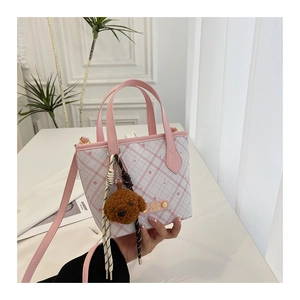 Detail view of pink plaid bucket bag with plush bear charm and COIN 2DN logo