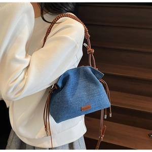 Detailed shot of denim bucket bag showing brown leather knotted strap and tassel accents