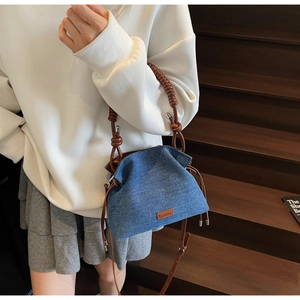 Detail of denim bucket bag with pleated design and brown braided leather handle