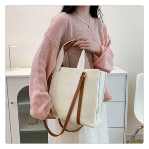Détail d'un sac cabas en toile avec bandoulières en cuir porté par un mannequin