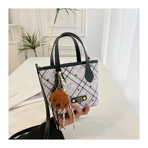 Detail of checkered bucket bag with brand logo and cute teddy bear charm accessory