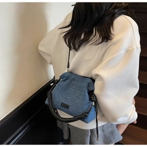 Detailed view of a blue denim bucket bag featuring a unique black spiral top handle