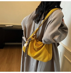 Detailed side view of yellow suede hobo bag with bohemian tassel charm on model