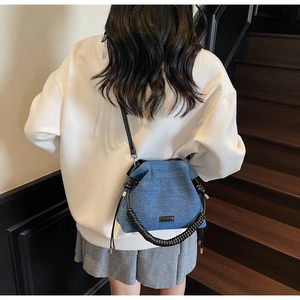 Detail of blue denim bucket bag with black spiral handle and drawstring pleat design