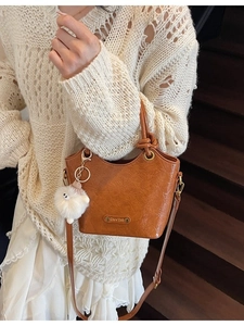 Brown crinkled leather bucket bag with top handle and cute plush charm on white sweater