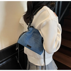 Detail view of denim bucket bag showing black spiral handle and drawstring closure