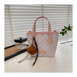 Detail of pink plaid bucket bag featuring a cute plush bear charm and metal logo plaque