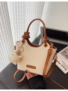Retro cream pleated bucket bag with brown handle and cute plush charm on a desk