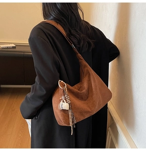 Detail of a brown suede hobo bag featuring a white coffee cup charm and woven lanyard