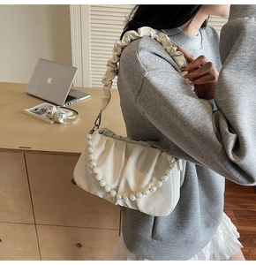Détail du sac nuage plissé blanc avec chaîne de perles élégante sur le bras du modèle