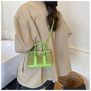 Detail of green mini tote bag with suede texture and leather handles worn by model
