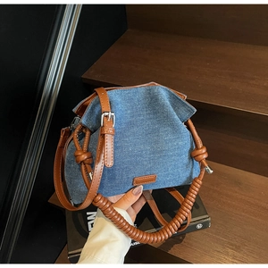 Close-up of denim bucket bag featuring woven rope handle and brown leather strap