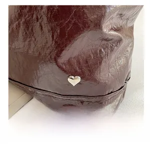 Detailed macro of dark brown glossy wrinkled leather bag with silver heart metal charm