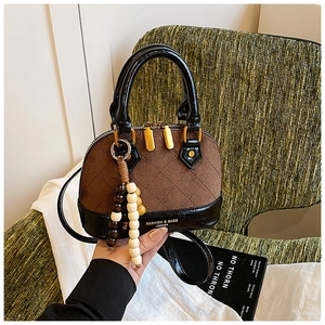 Detail view of contrast stitching shell bag with gold hardware and colorful beaded charm