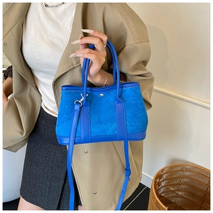 Detail of blue suede tote bag with leather trim and silver buckles on a trench coat