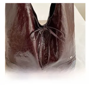 Detail showing deep burgundy glossy pleated leather tote with bow and heart logo
