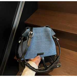 Close-up of blue denim bucket bag with black spiral handle and silver metal buckles