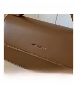 Detail shot of brown leather handbag featuring a brand logo and neat stitching