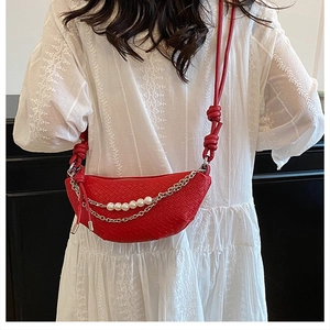 Dettaglio della borsa a mezzaluna rossa intrecciata con perle e catena su una modella