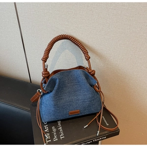 Detail of denim bucket bag with thick twisted handle and drawstring closure on a book