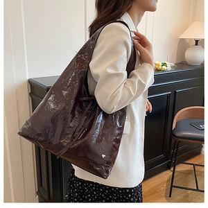 Detail of a large dark brown gloss tote bag styled with a white blazer on a model