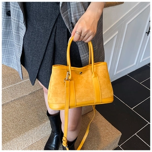 Close-up of bright yellow suede tote bag with leather trim held by model on stairs