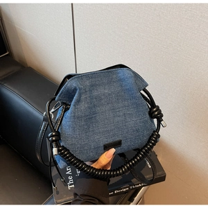 Detail of blue denim bucket bag with unique black spiral handle and crossbody strap